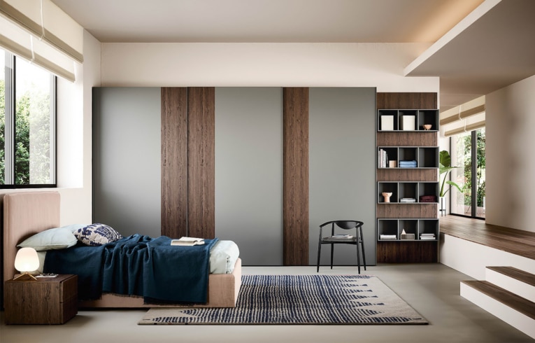 dressing moderne à portes coulissantes plaqué bois et couleur gris mat encastré dans un mur conjoint à une bibliothèque équipée de tablette de rangement