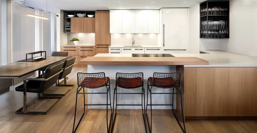 Cuisine design italienne de luxe couleur blanche et bois avec plan de travail en céramique blanche disposé en épis et table de bar en bois avec trois chaises de bar