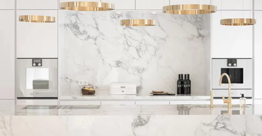 Cuisine d'exception avec plan de travail et crédences en granit blanc, électroménagers intégrés dans façades et îlot central avec mitigeur couleur or